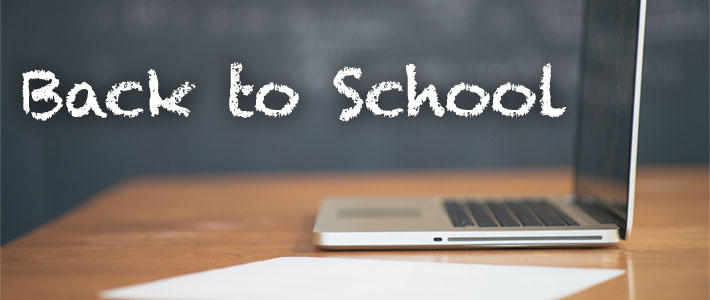 Laptop sitting on a desk with the words Back to School written in chalk